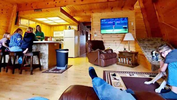 Interior acogedor de una cabaña de madera con una cocina, barra y sala de estar con televisor.