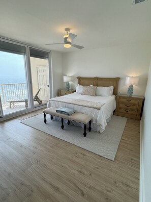 Relax in a spacious bedroom with a large bed, comfortable bench, and sliding glass door leading to a balcony with ocean views.