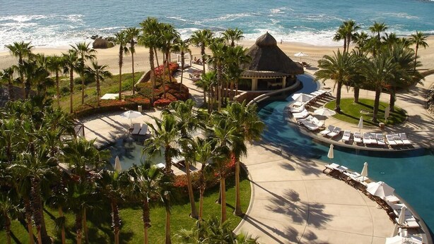 Un resort con piscina, palmeras y vista al mar.