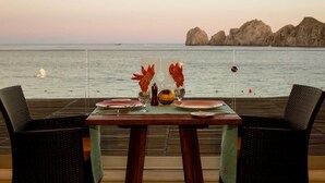 Una mesa de comedor con vista al mar y formaciones rocosas al fondo.