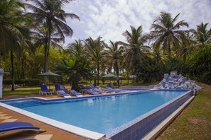 A swimming pool with blue water, surrounded by palm trees and lounge chairs.