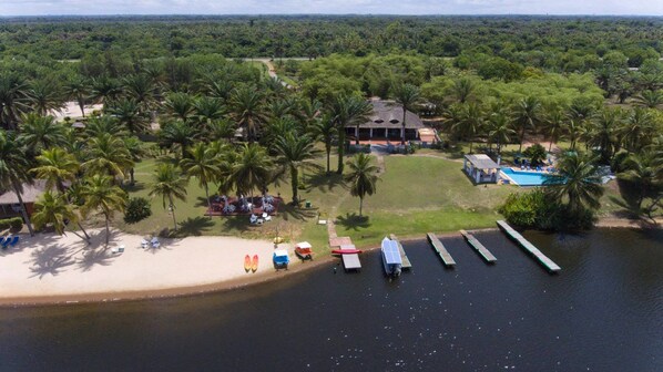 An aerial view of a resort with a beach, palm trees, a swimming pool, and docked boats.