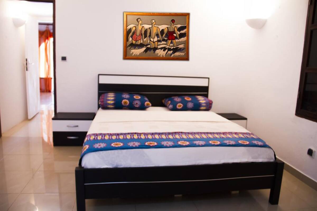 Ein Schlafzimmer mit einem Bett, Kissen, einem Nachttisch und einem Wandbild.