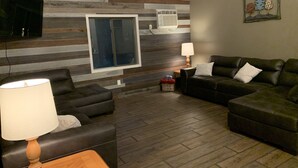 Un salón con un sofá modular, suelo de madera, televisor montado en la pared y aire acondicionado instalado.