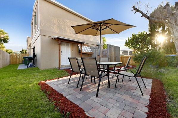 A patio with a table and chairs, a large umbrella, and a brick floor.