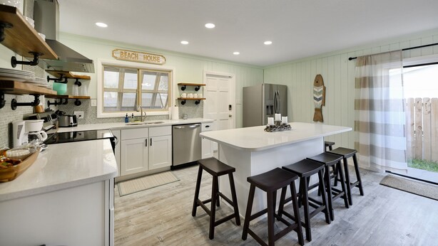 A kitchen with a large island, bar stools, a refrigerator, and a sign that reads "BEACH HOUSE".