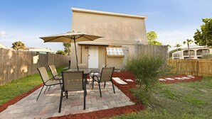 A patio area with a table and chairs, a wooden fence, and a building in the background.