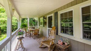 A covered porch with wooden furniture, potted plants, and a birdhouse.