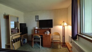 A hotel room with a desk, chair, television, and a lamp. - King Bed - MCM Style- Backyard View (Spring Green)