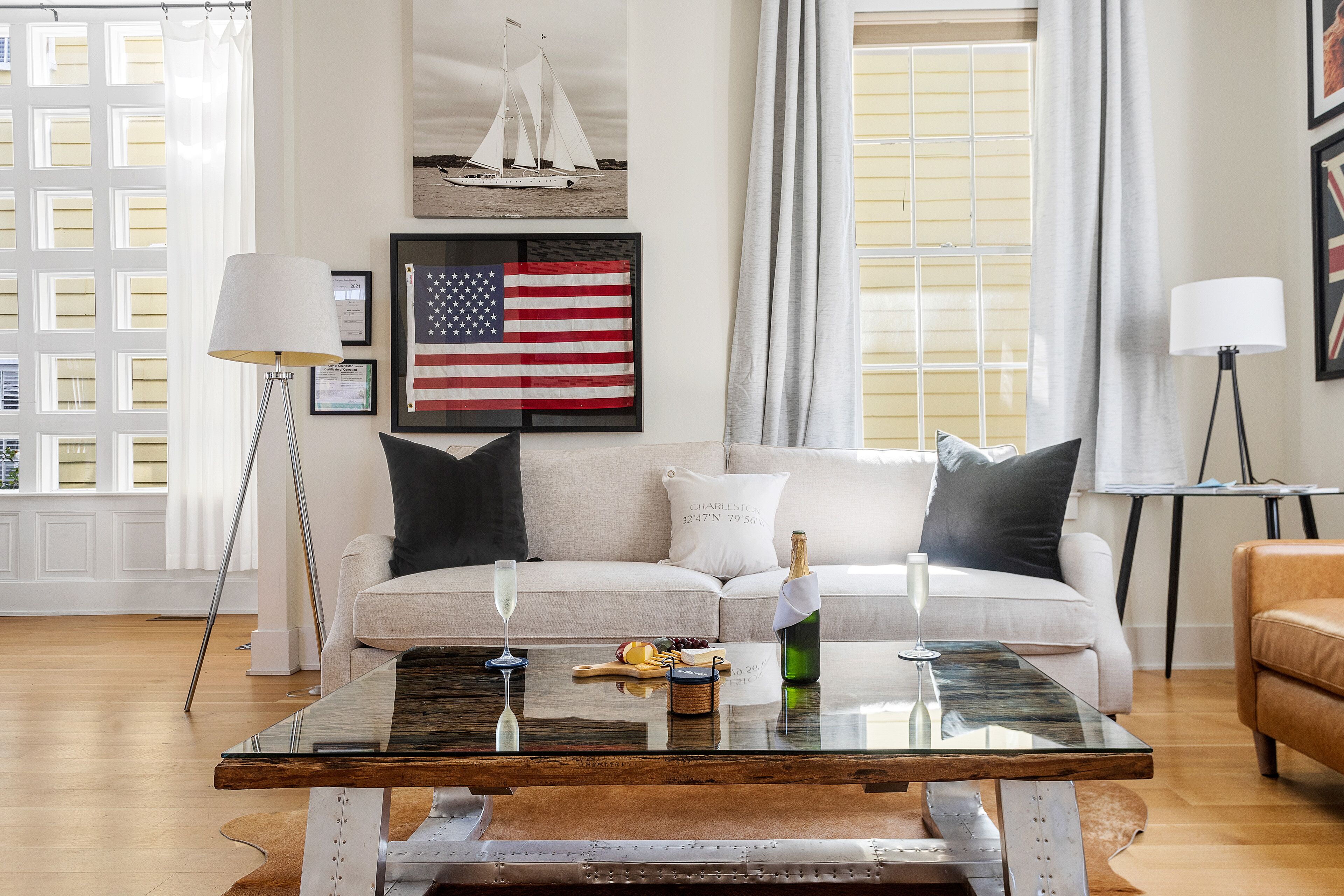 A living room with a sofa, a glass coffee table, and a framed American flag.