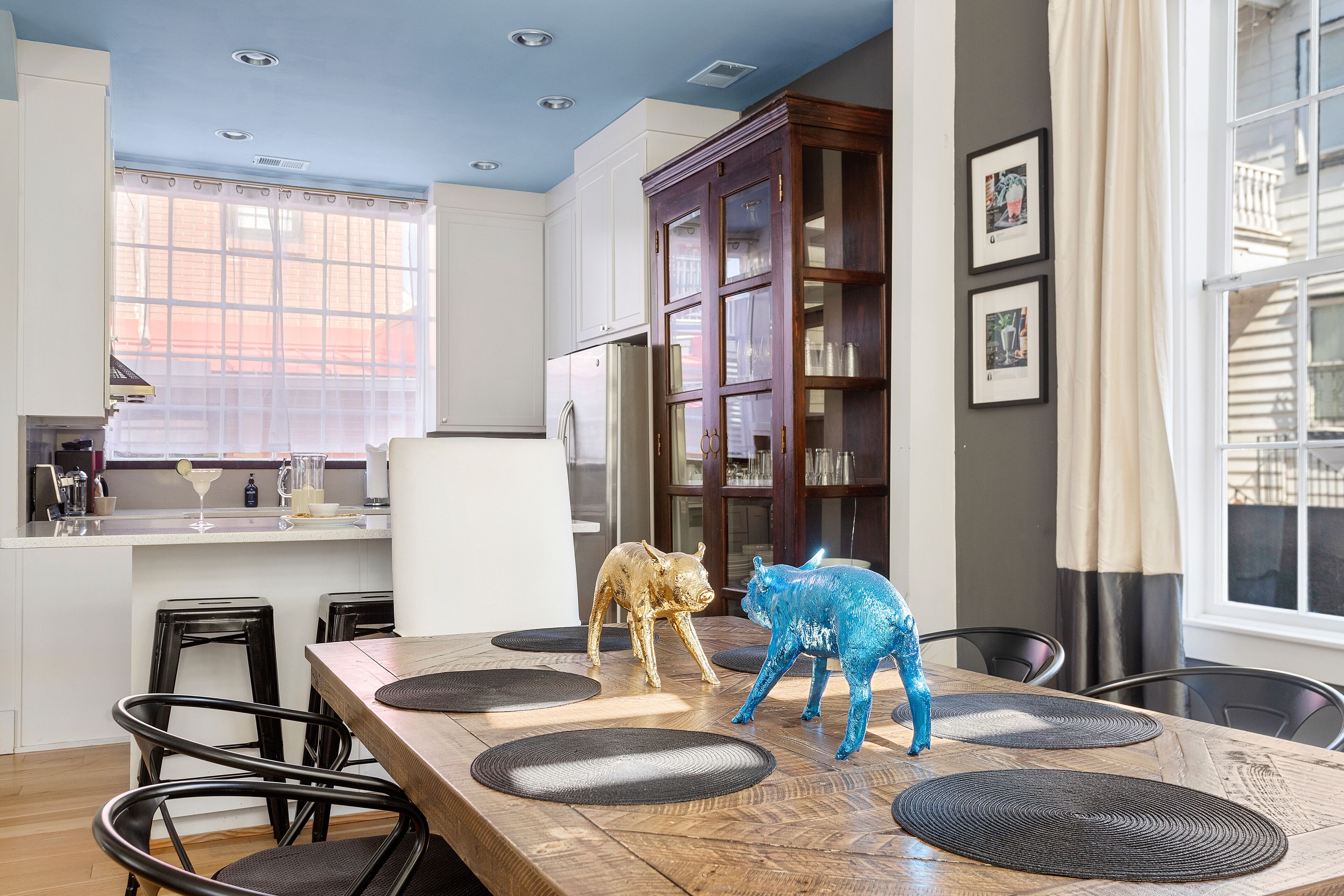 Een moderne keuken met een eethoek, met een houten tafel, zwarte stoelen en decoratieve varkensbeeldjes.