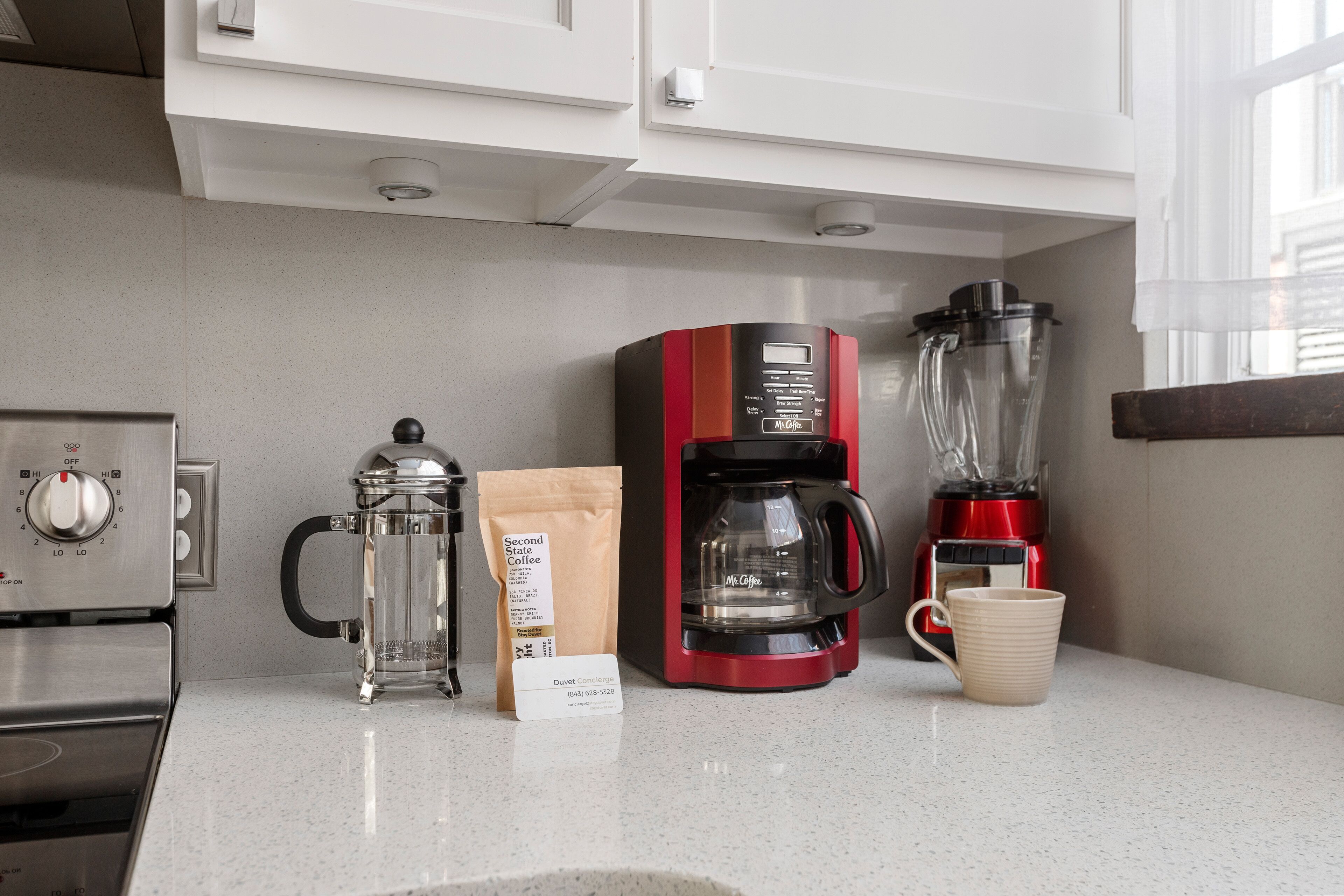 Una cocina con cafetera, licuadora, molinillo de café y una bolsa de café.