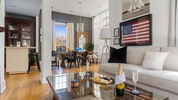 A modern living room with a glass coffee table, a sofa, and a dining area in the background. - Embrace Comfort and Convenience | Hibiscus House (Charleston)