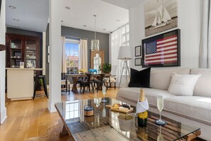 A modern living room with a glass coffee table, a sofa, and a dining area in the background. - Embrace Comfort and Convenience | Hibiscus House (Charleston)