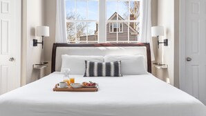 A neatly made bed with white linens, a tray with breakfast items, and a window with a view of a house and trees. - Embrace Comfort and Convenience | Hibiscus House (Charleston)
