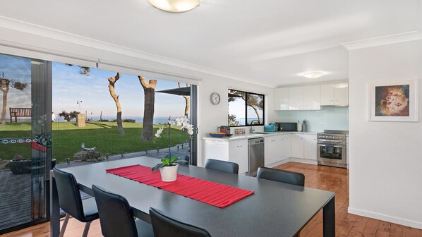 Une cuisine moderne avec des meubles blancs, un coin repas agrémenté d’un set de table rouge, et une vue sur un espace verdoyant avec des arbres.