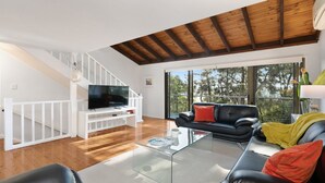 A modern living room with a TV, black leather sofa, and a staircase. - Amazing views and short walk to beach (Copacabana)