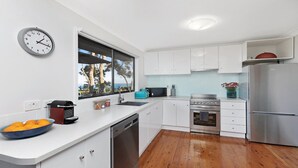 A modern kitchen with white cabinets, a stainless steel refrigerator, a built-in oven, and a window with a view of trees and the sky. - Amazing views and short walk to beach (Copacabana)