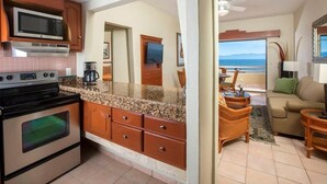 Una cocina con microondas, estufa y horno, un comedor con mesa y sillas, y vista al océano a través de una puerta.