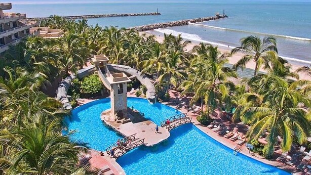 Un resort con una piscina grande, palmeras y vistas al océano.