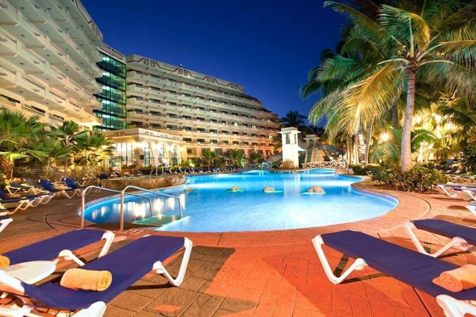 Un espace piscine d’hôtel avec des chaises longues et des palmiers.