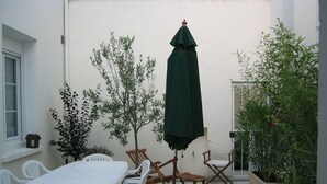 Een terras met een witte tafel en stoelen, een groene parasol en potplanten.