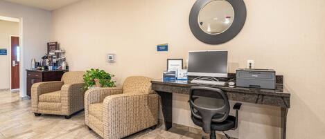A hotel room with a desk, two armchairs, a computer, and a printer.
