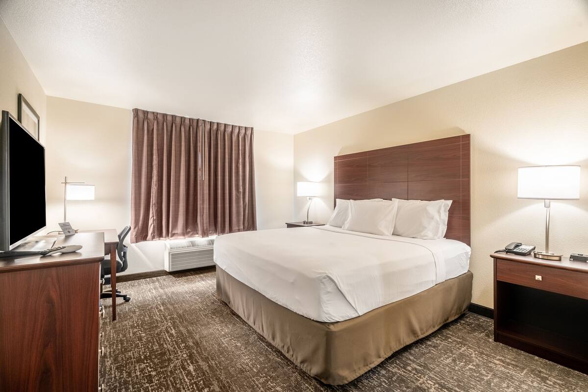 A hotel room with a large bed, a desk with a TV, a chair, and a lamp.