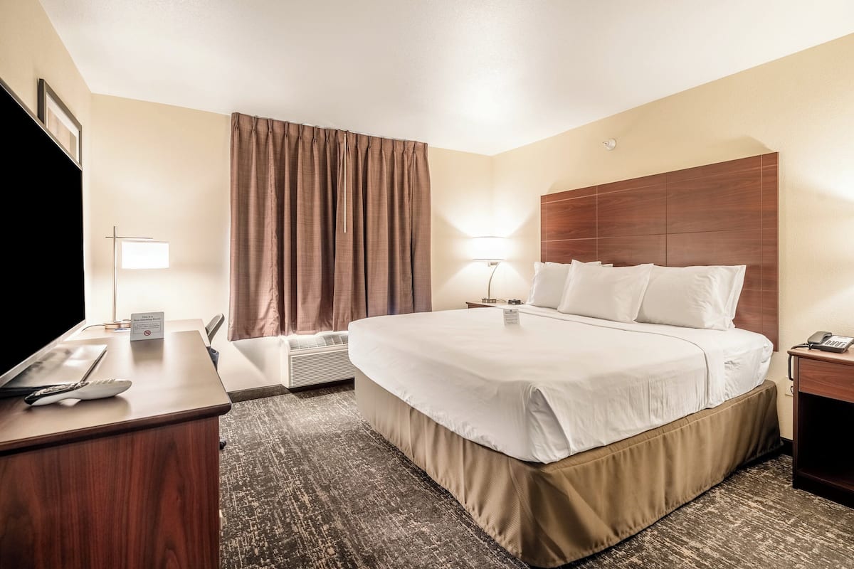 A hotel room with a large bed, a desk with a telephone, a lamp, and a window with curtains.