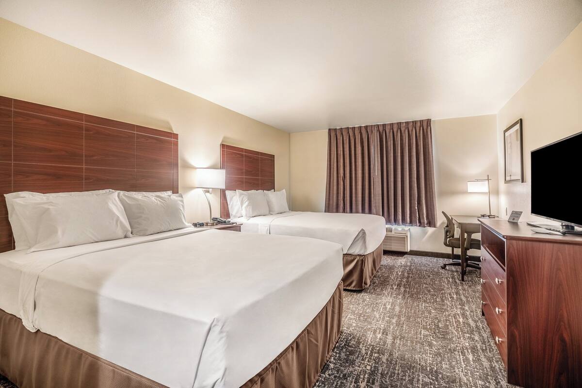 A hotel room with two beds, a desk, a chair, a TV, and a large window with curtains.