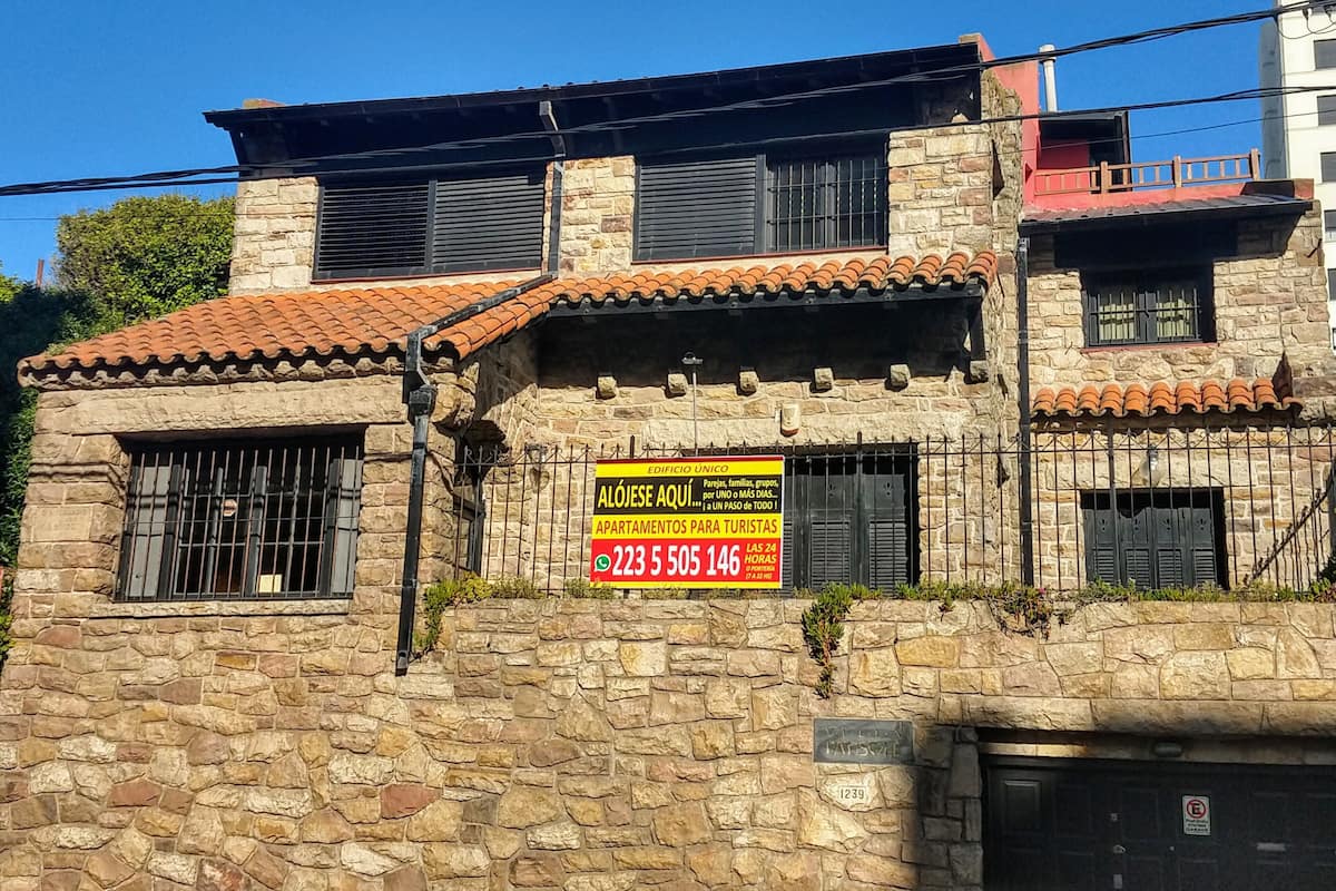 A stone building with a tiled roof, a sign advertising tourist apartments, and a visible address number.