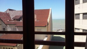 A view through a window of a building with red-tiled roofs, a balcony, and a view of the sea. - Edificio Único (Mar del Plata)