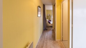 Passadís estret amb parets grogues i un sòl de fusta, que condueix a una habitació amb un llit i una cadira.