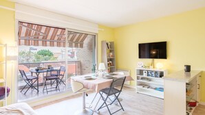 Una habitació ampla i de color groc clar amb zona de menjador, televisió i prestatgeria.