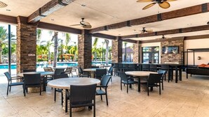 A spacious outdoor dining area with multiple tables and chairs, a pool in the background, and a stone wall. - Your Disney Family Vacation Resort Home With Private Pool/TikiBar (Davenport)