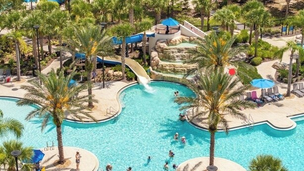 A large outdoor swimming pool surrounded by palm trees and a water slide. - Your Disney Family Vacation Resort Home With Private Pool/TikiBar (Davenport)
