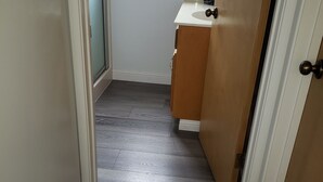 A narrow hallway with a wooden floor, a white door on the left, and a bathroom with a sink and mirror on the right. - Cottage By The Sea At Cayucos where serenity is found, 3 minute walk to beach (Cayucos)