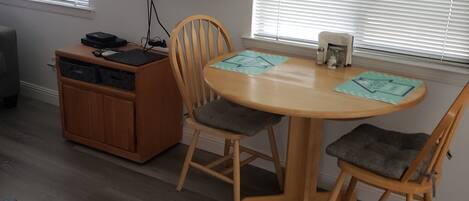 A dining area with a round table and four chairs, a television mounted on the wall, and a wooden cabinet with drawers.