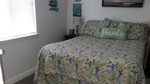 A bedroom with a floral bedspread, a nightstand with a lamp, and a framed picture on the wall. - Cottage By The Sea At Cayucos where serenity is found, 3 minute walk to beach (Cayucos)
