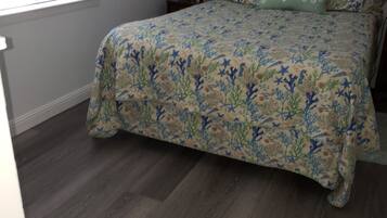 Une chambre à coucher avec une couvre-lit à motifs floraux, une table de chevet avec une lampe et un tableau encadré au mur.