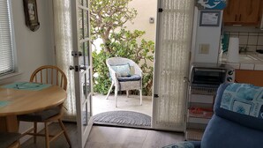 A living room with a sofa, a dining table with chairs, a kitchen area with a toaster, and a sliding glass door leading to a patio with a chair and a tree. - Cottage By The Sea At Cayucos where serenity is found, 3 minute walk to beach (Cayucos)