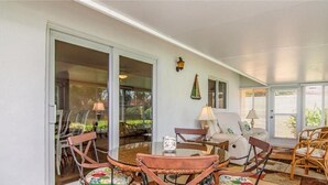 Un patio techado con puerta de vidrio que da a un jardín, mobiliario de mimbre y una lámpara.