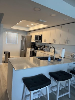 A modern kitchen with stainless steel appliances, white cabinets, and a central island with bar stools. - Gulf View 103 - Anna Maria Island - Condo 2 Bedroom/ 2 Bath ocean view, maximum occupancy of 4 people. (Bradenton Beach)