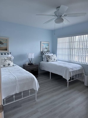 A bedroom with two beds, a ceiling fan, and a window with blinds. - Gulf View 103 - Anna Maria Island - Condo 2 Bedroom/ 2 Bath ocean view, maximum occupancy of 4 people. (Bradenton Beach)