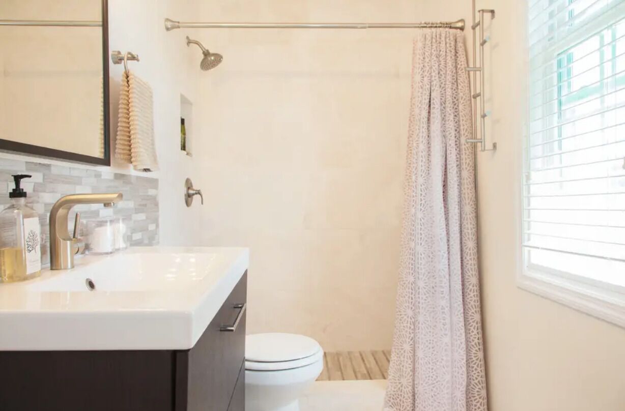 A bathroom with a white sink, a mirror, a shower curtain, and a toilet.