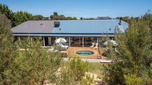 Une maison moderne dotée d’un patio couvert, d’une piscine et offrant une vue sur les arbres environnants.