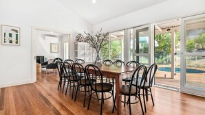 Un vaste espace dédié à la salle à manger, avec une table et des chaises en bois, de grandes fenêtres et une vue sur une piscine.