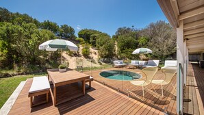 Une terrasse en bois avec une piscine, du mobilier d’extérieur et des parasols.