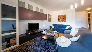 Un salon moderne avec un téléviseur à écran plat, une table basse, un canapé bleu et un tapis à motifs.