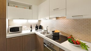 Une cuisine moderne avec des armoires blanches, un four à micro-ondes, un évier et une cuisinière. Un saladier rempli de légumes est posé sur le comptoir.